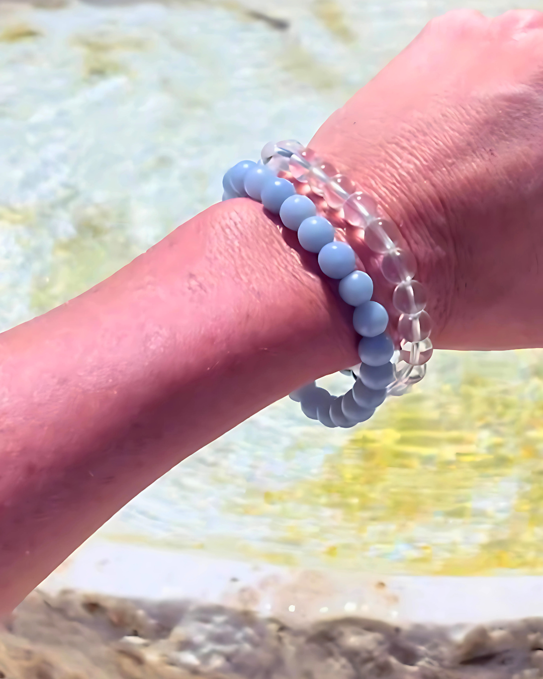 Close-up of a hand wearing two bracelets with a blurred beach background