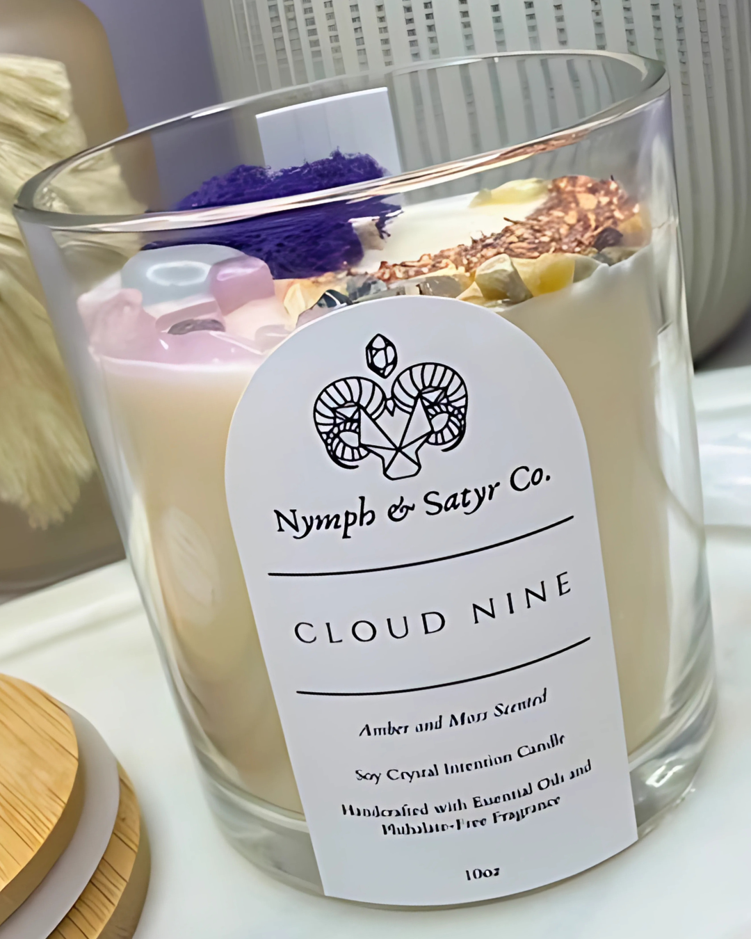 Candle labeled 'Nymph & Satyr Co. Cloud Nine' with decorative elements inside the glass.