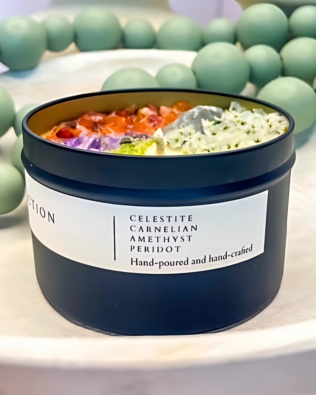 Candle with colorful interior and label on a white surface with green beads in the background