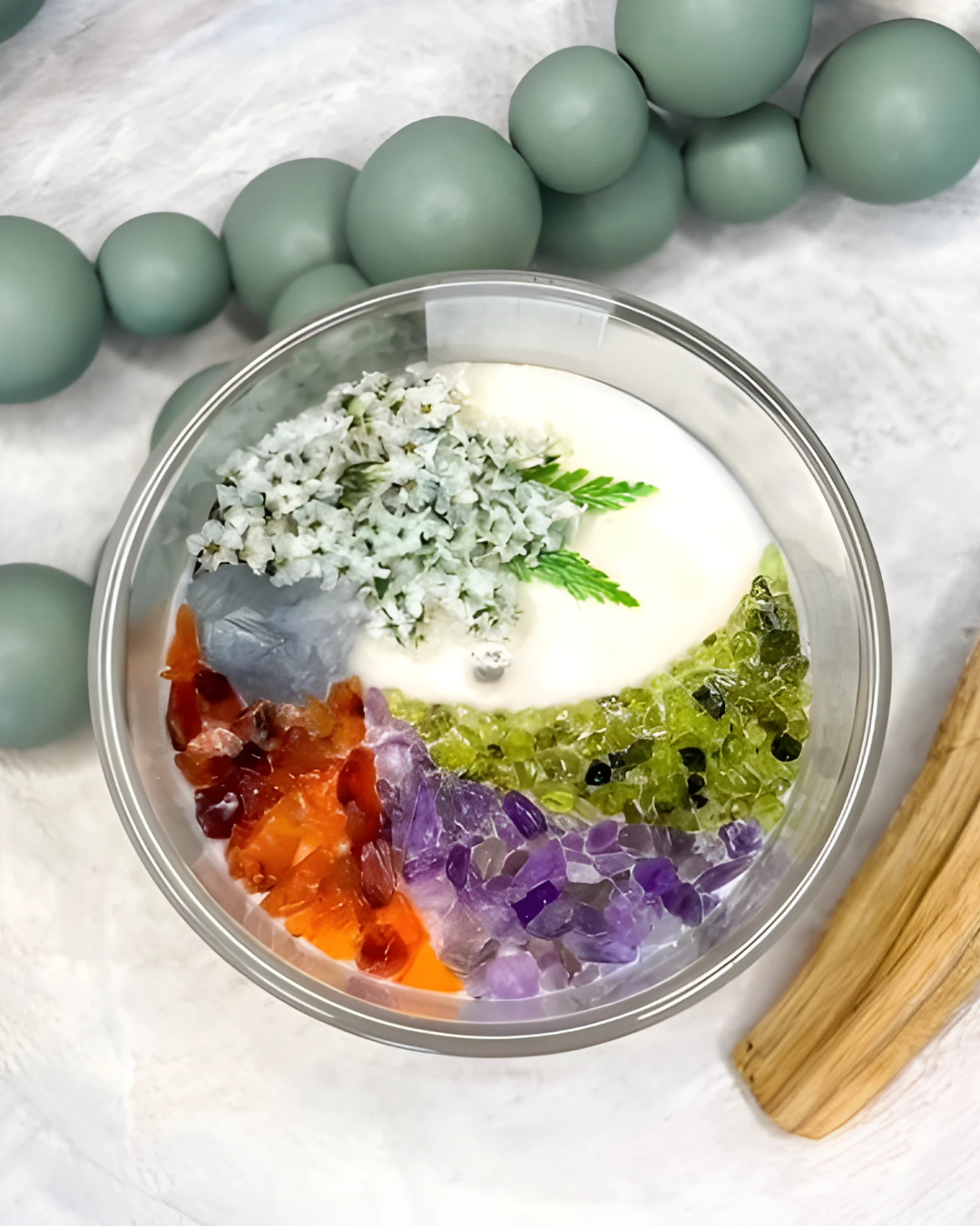 Decorative bowl with colorful crystals and a wooden tool on a white background