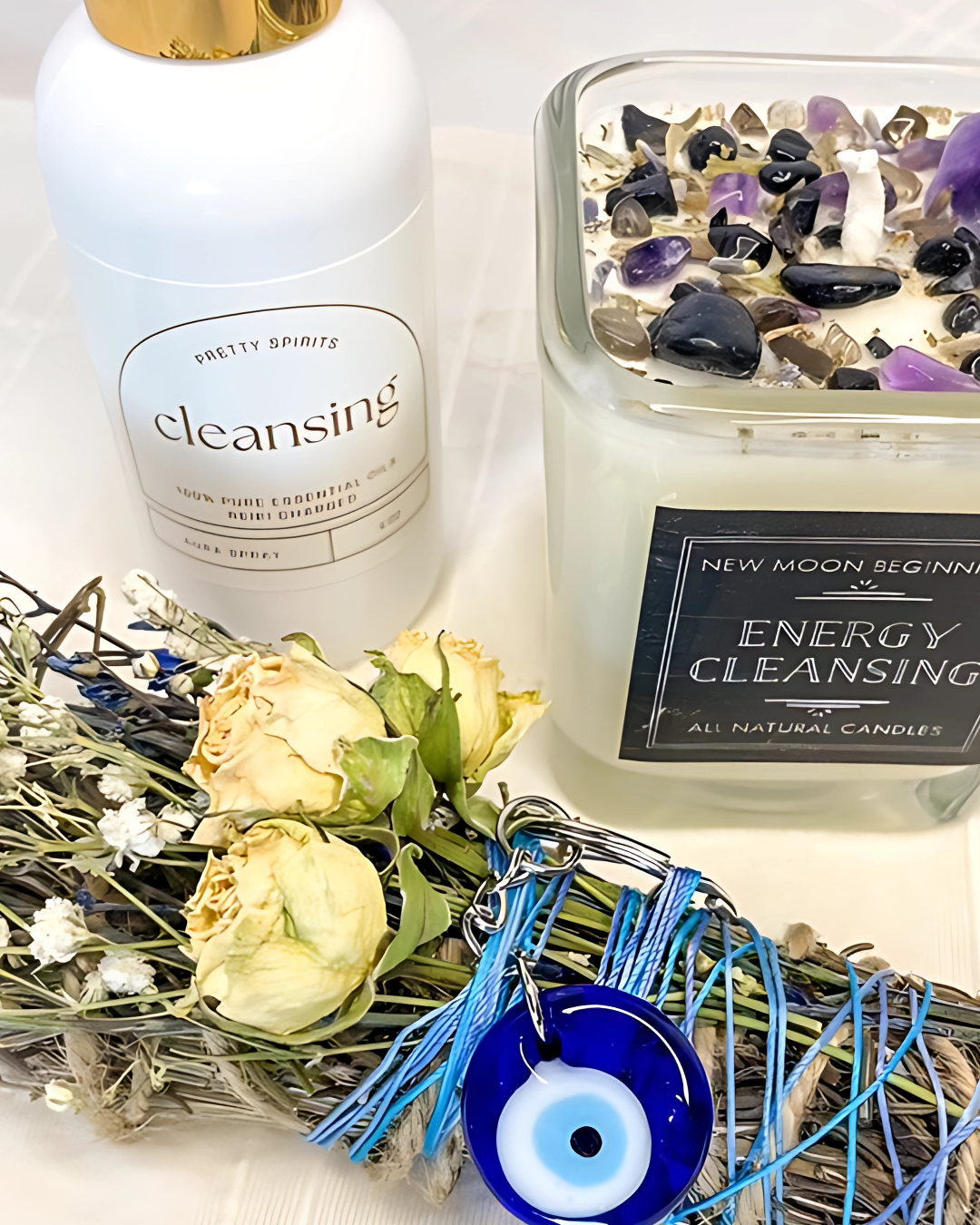 Cleansing bottle, energy cleansing candle, dried flowers, and evil eye charm on a white surface
