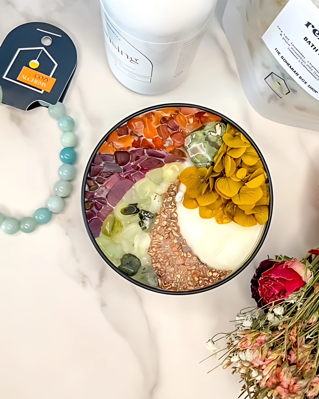 Colorful bowl with various items on a light surface, including a necklace and flowers.