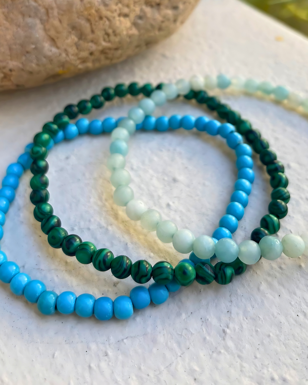 Set of three beaded bracelets in blue and green on a textured surface