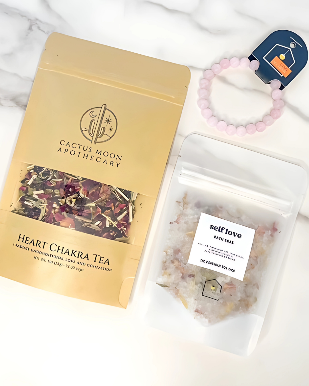 Cactus Moon Apothecary heart chakra tea package, self love bath salts, and a bracelet on a white surface.