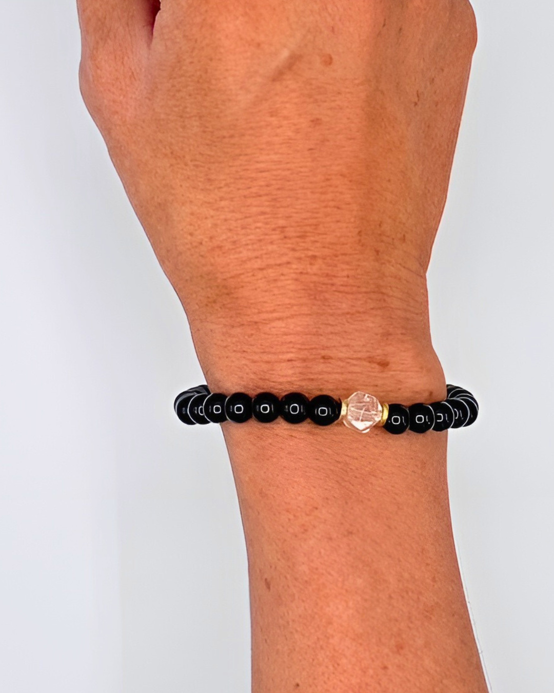 Black beaded bracelet with a clear crystal on a wrist against a white background