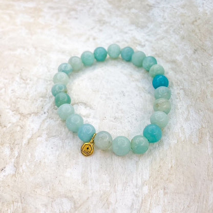 Beaded bracelet with a gold heart charm on a textured white surface