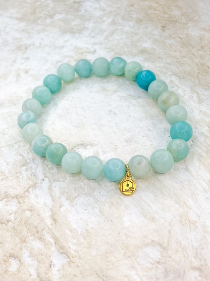 Turquoise beaded bracelet with a gold charm on a white textured background