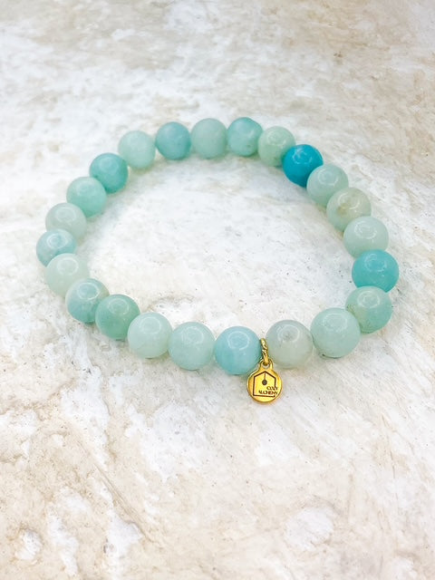 Turquoise beaded bracelet with a gold charm on a white textured background