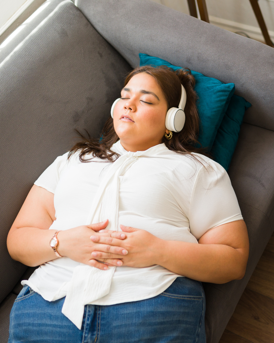 Woman wearing headphones and relaxing on a couch with a blue pillow.