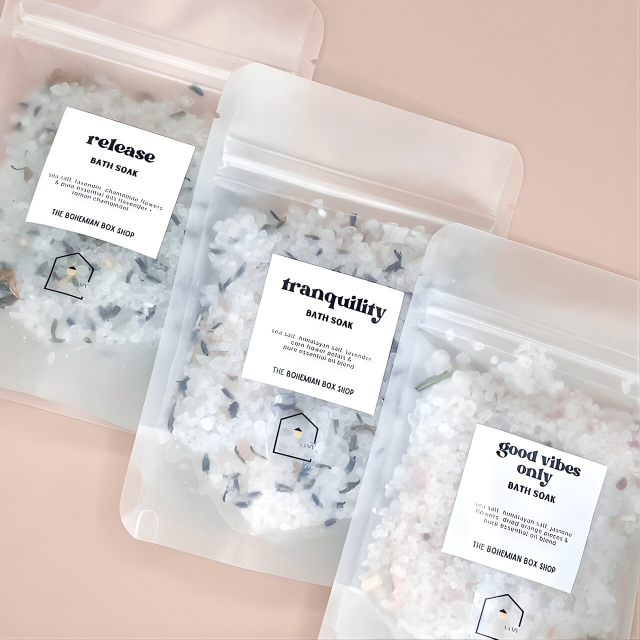 Three packages of bath soaks with labels on a light pink background