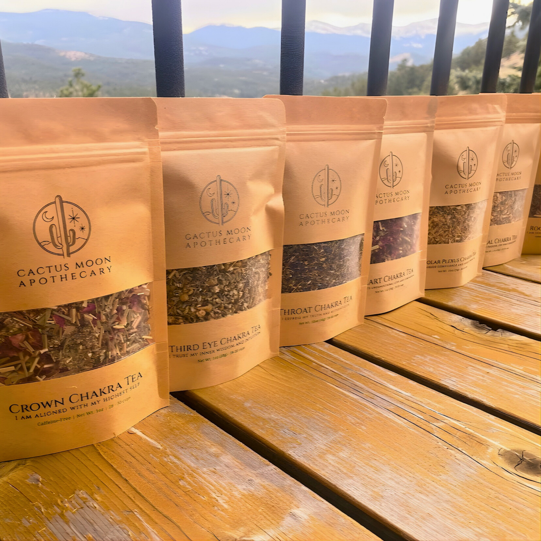 Row of Cactus Moon Apothecary tea packages on a wooden surface with a scenic background.