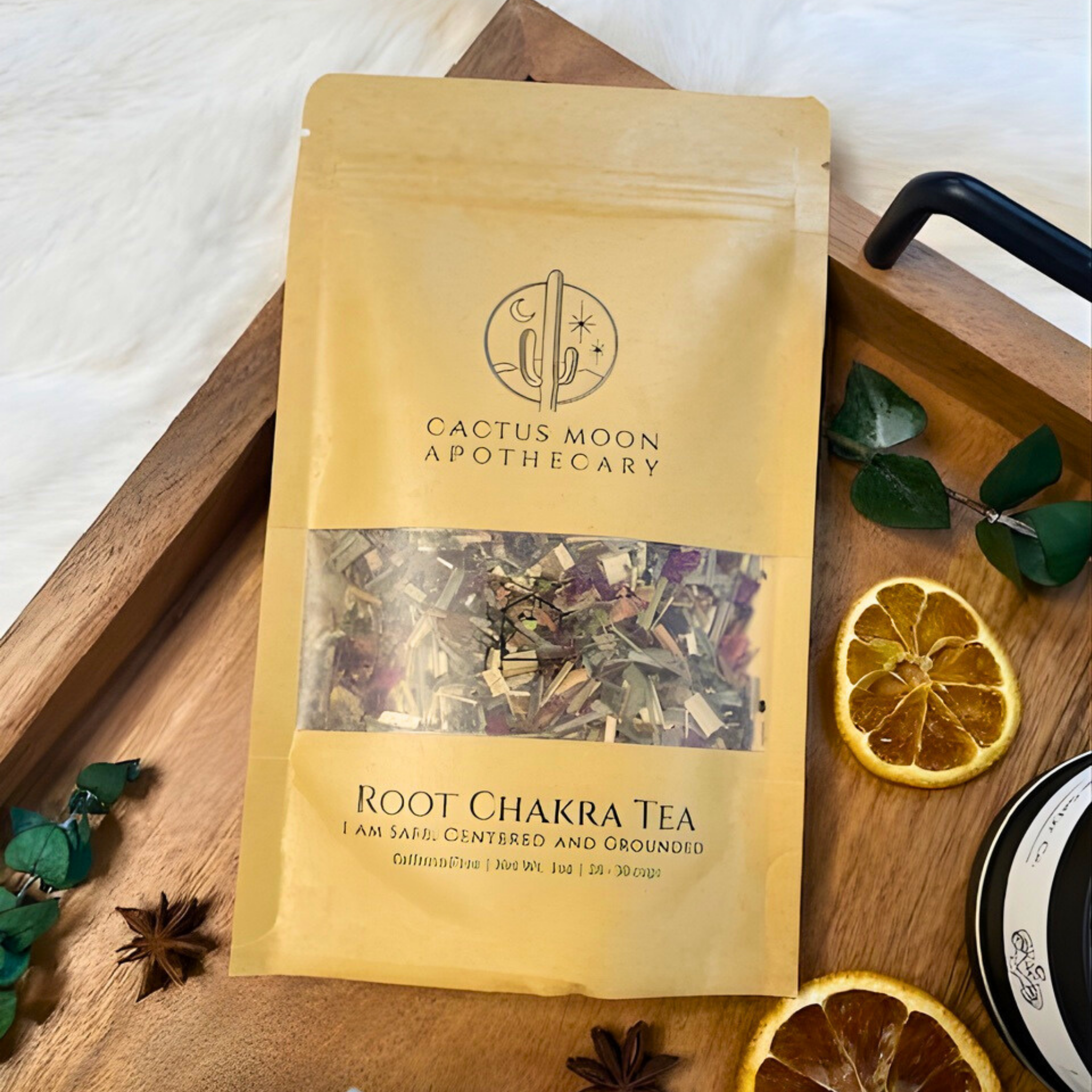 Bag of Root Chakra Tea from Cactus Moon Apothecary on a wooden tray with dried oranges and leaves.