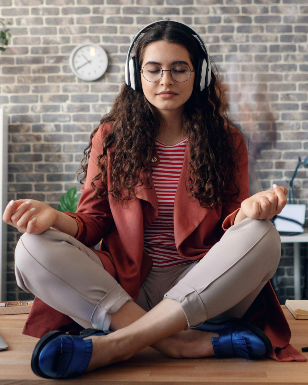 Person sitting cross-legged on a wooden floor with headphones on, in front of a brick wall.