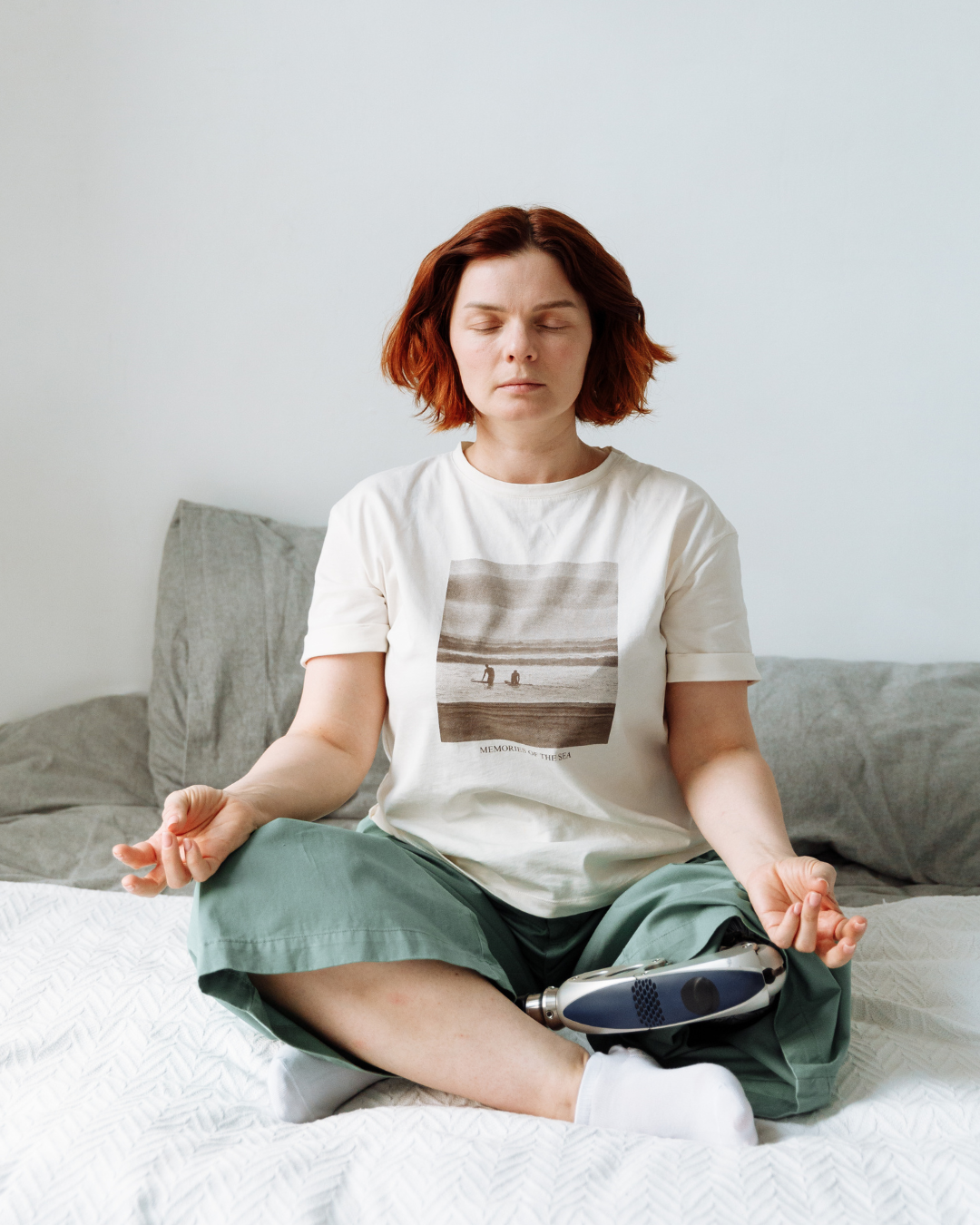 Person meditating on a bed with a white pillow and gray blanket.