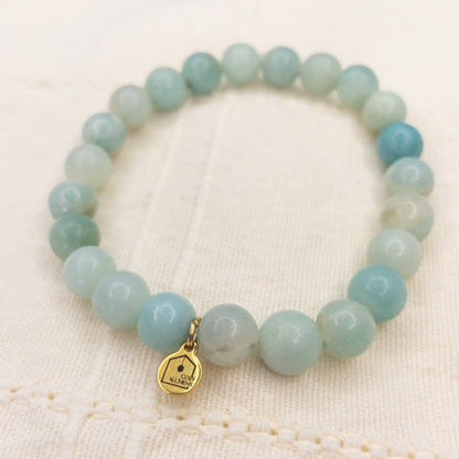 Light blue beaded bracelet with a gold charm on a beige fabric background