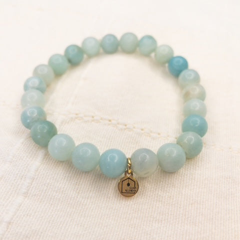 Light blue beaded bracelet with a gold tag on a white background