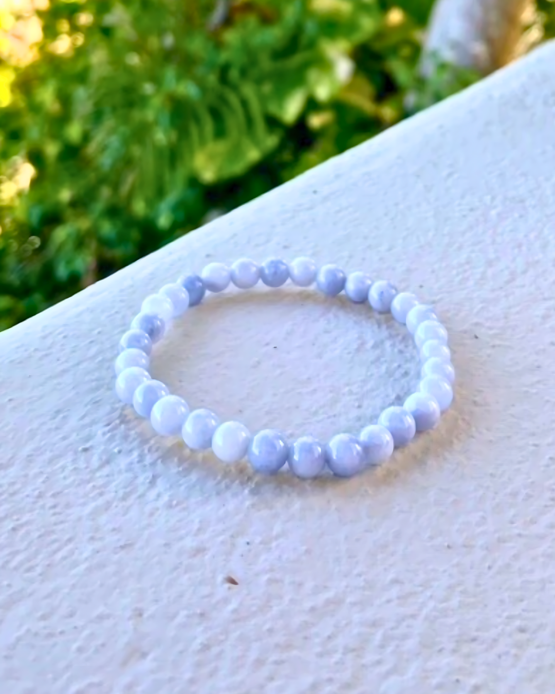 White beaded bracelet on a white surface with greenery in the background