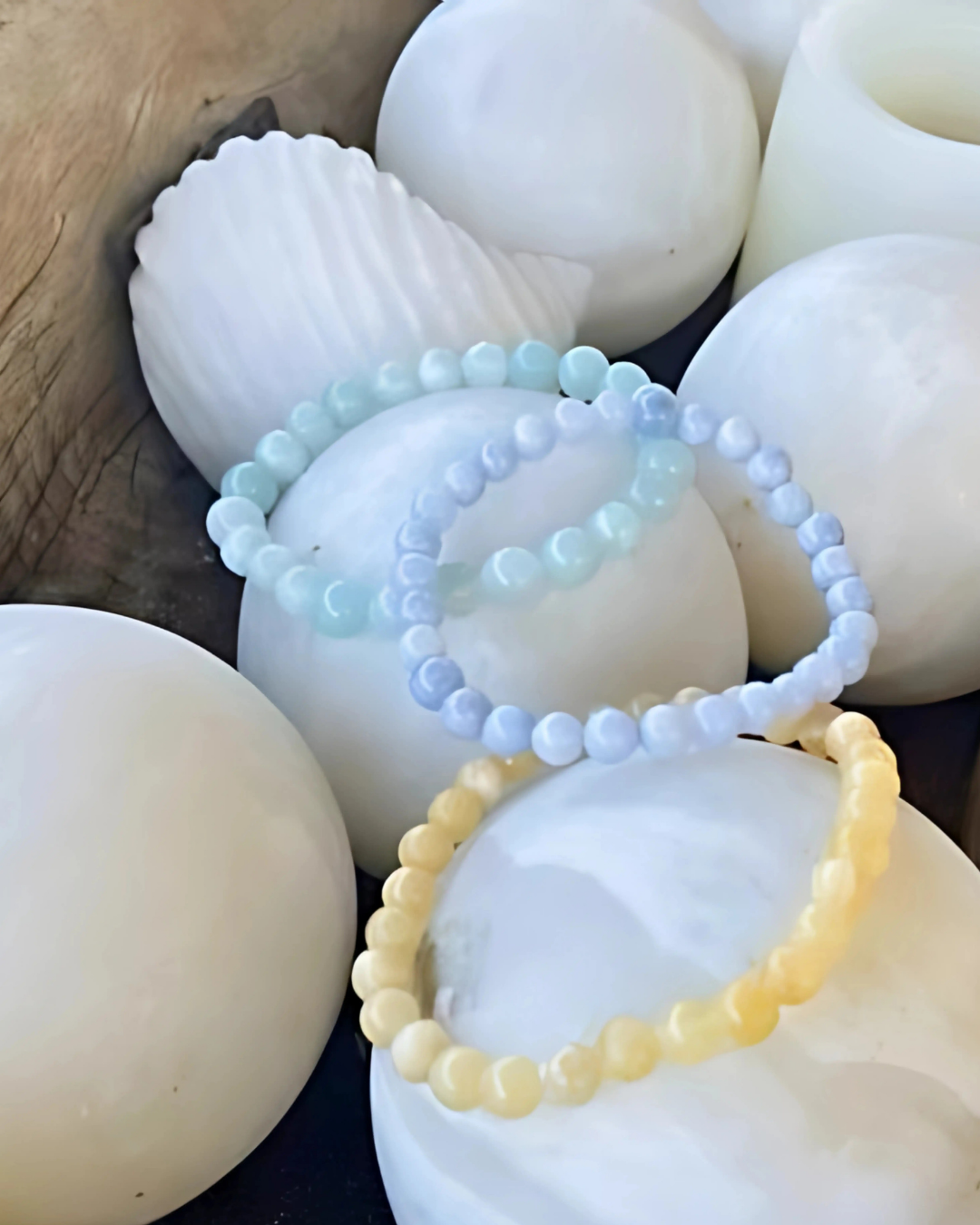 Three beaded bracelets in light blue, white, and yellow on seashells.