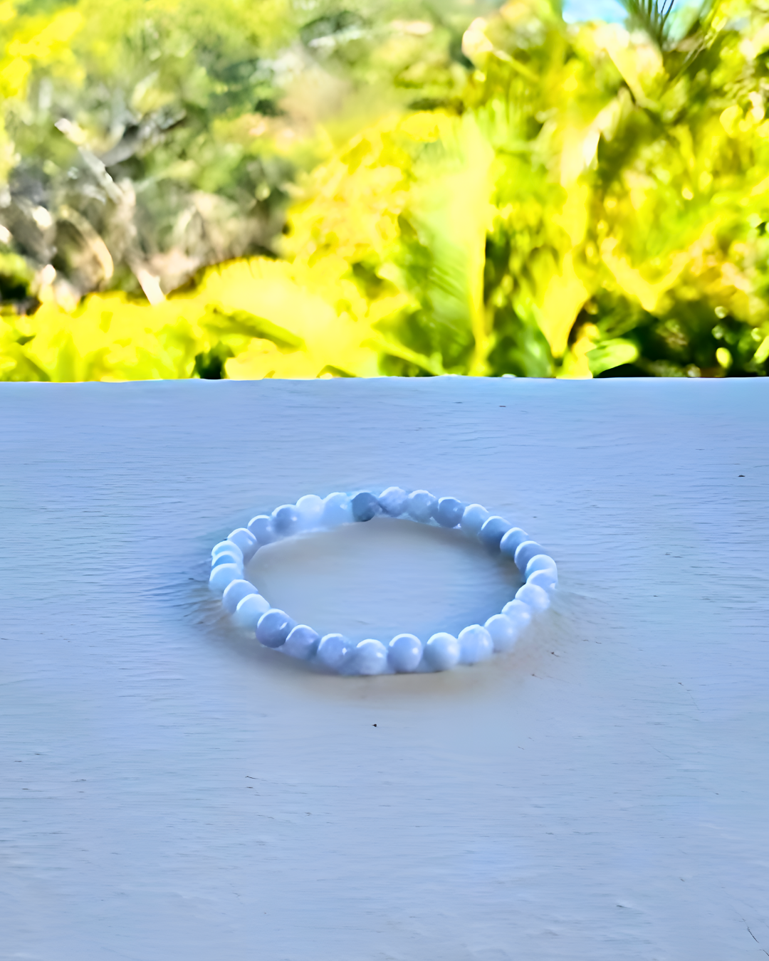 Blue beaded bracelet on a light blue surface with green foliage in the background