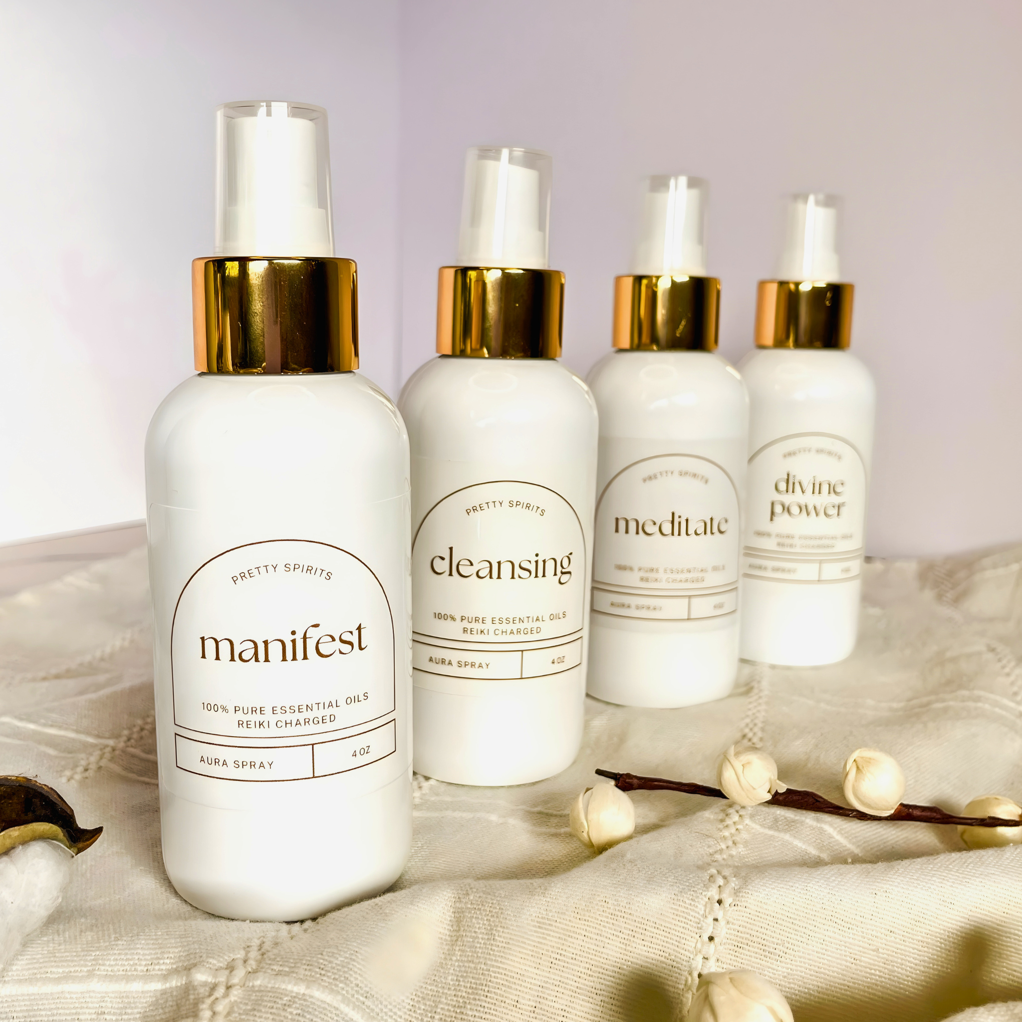 Four white bottles with gold caps labeled 'manifest', 'cleansing', 'meditate', and 'divine power' on a textured surface.