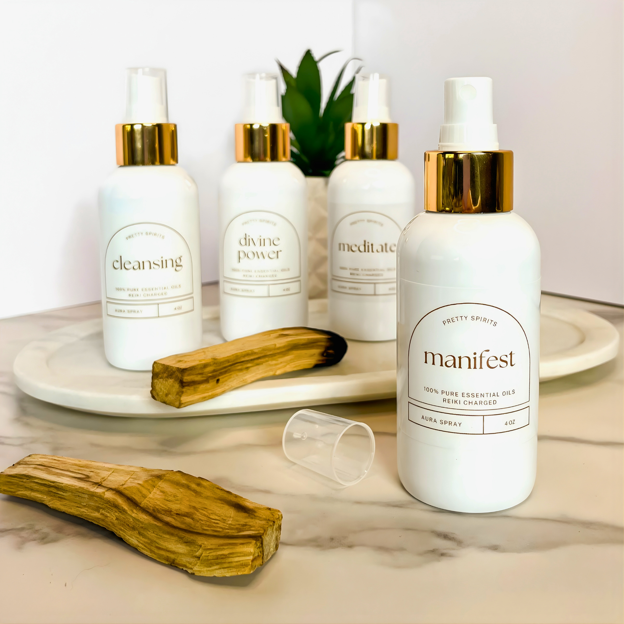 Set of white bottles with gold caps labeled 'cleansing', 'divine power', 'meditate', and 'manifest' on a marble surface.
