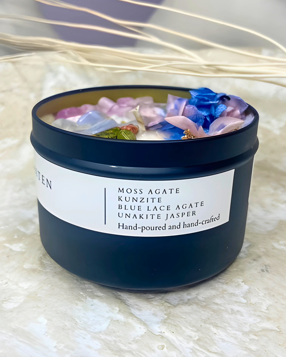 Candle in a dark blue container with colorful stones and flowers on a light background