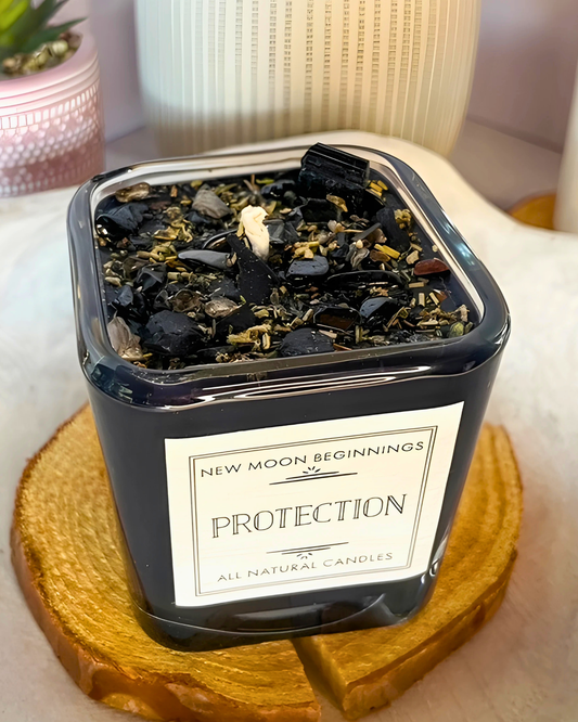 Candle in a black container labeled 'New Moon Beginnings Protection' on a wooden coaster.
