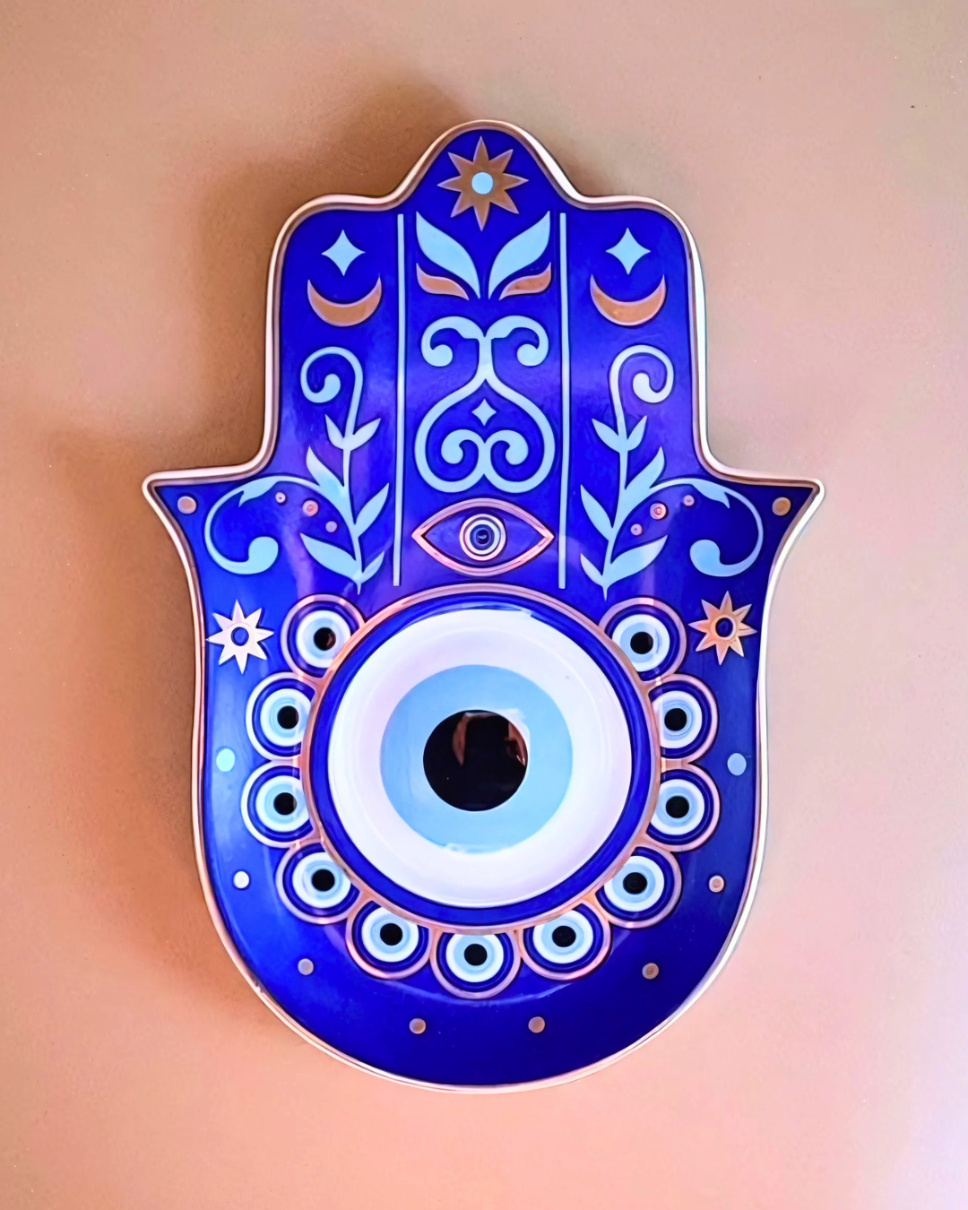 Decorative Hamsa hand with blue and white patterns on a pink background