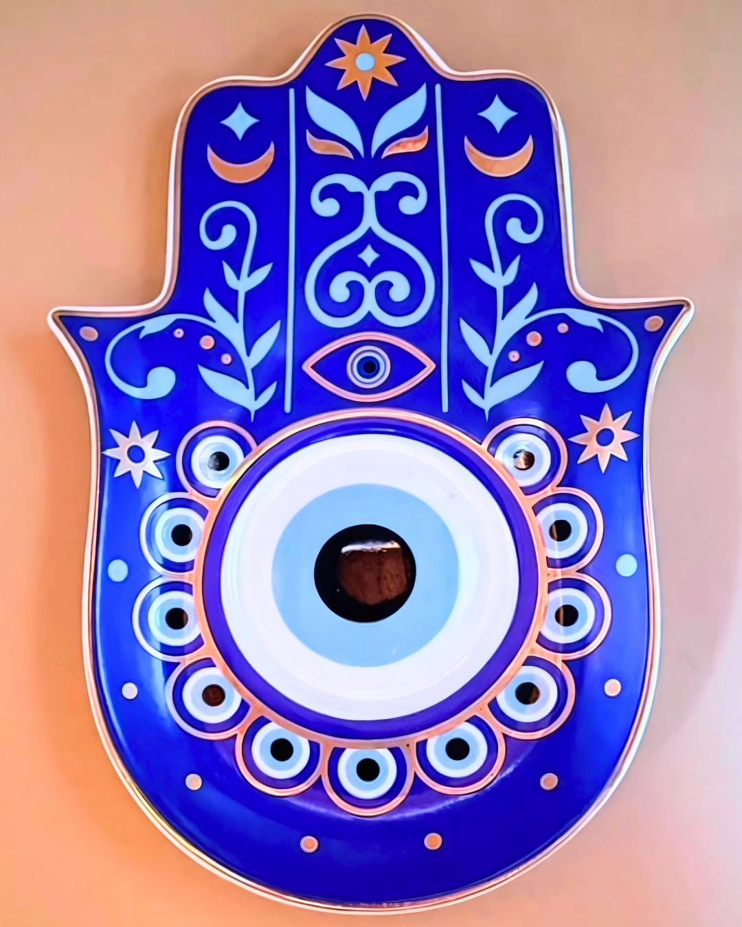 Decorative Hamsa hand with blue and white colors on a peach background