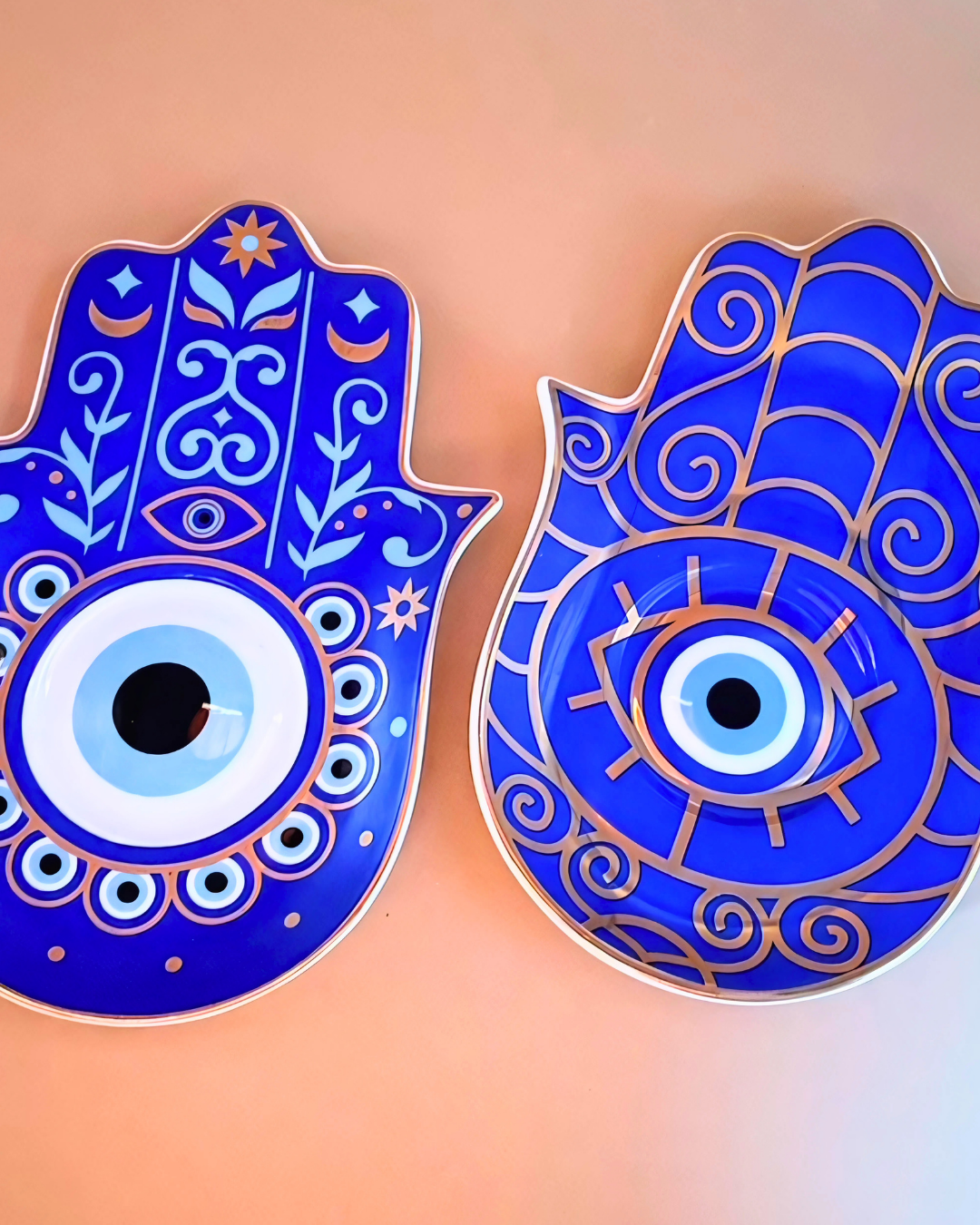 Two blue Hamsa hand decor items with eye design on a peach background