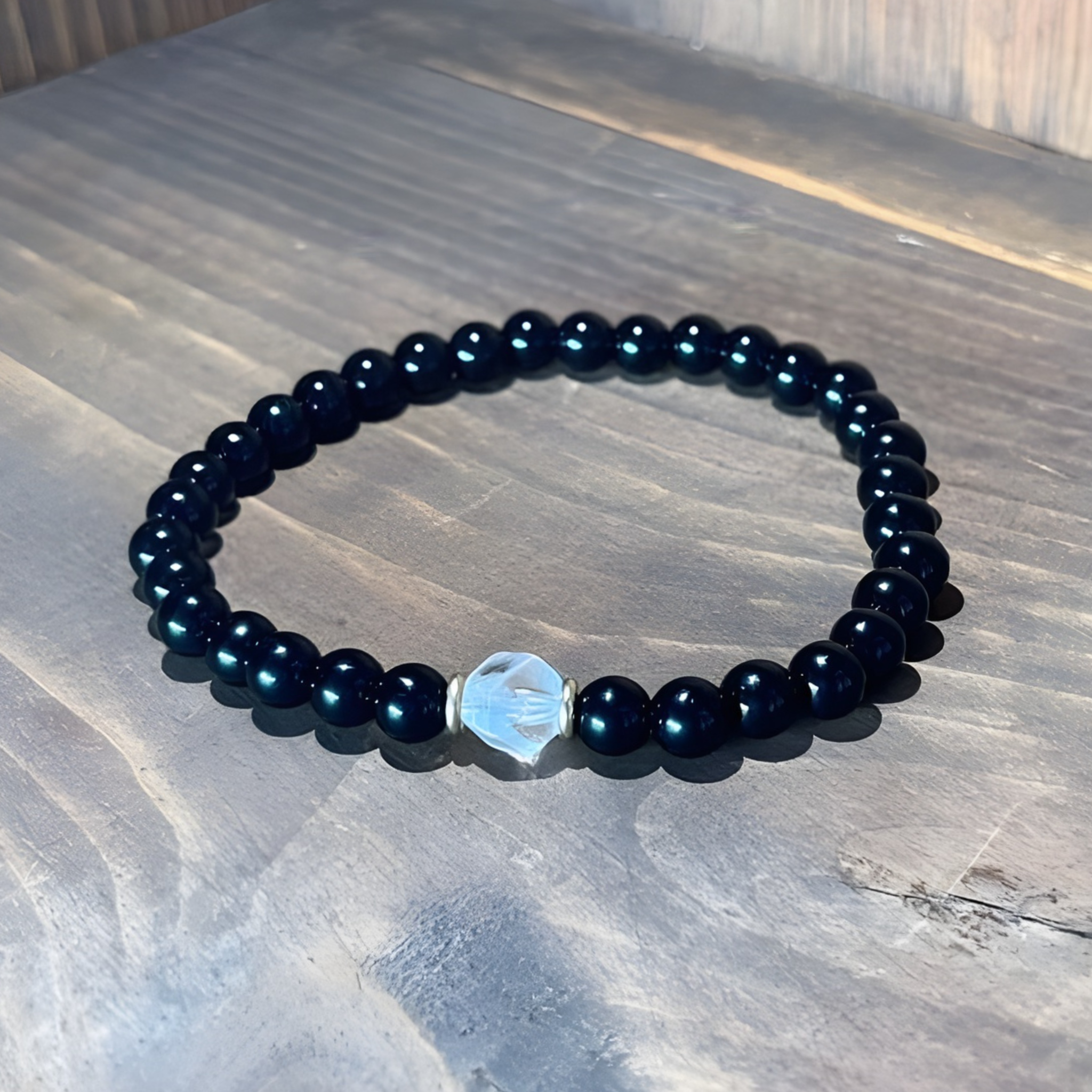 Black beaded bracelet with a silver hexagonal charm on a marble surface