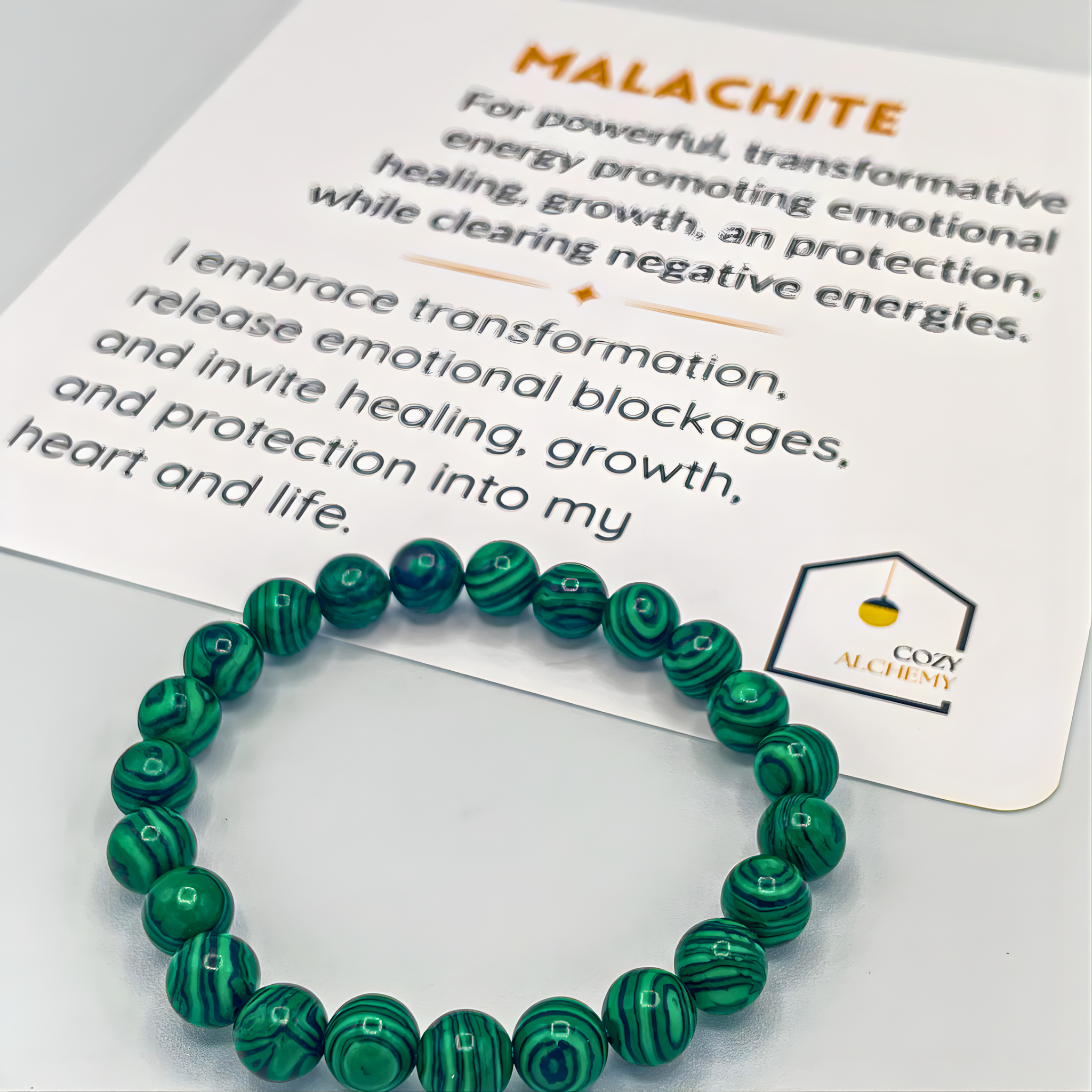 Green beaded bracelet on a Cozy Alchemy branded card with text about malachite.