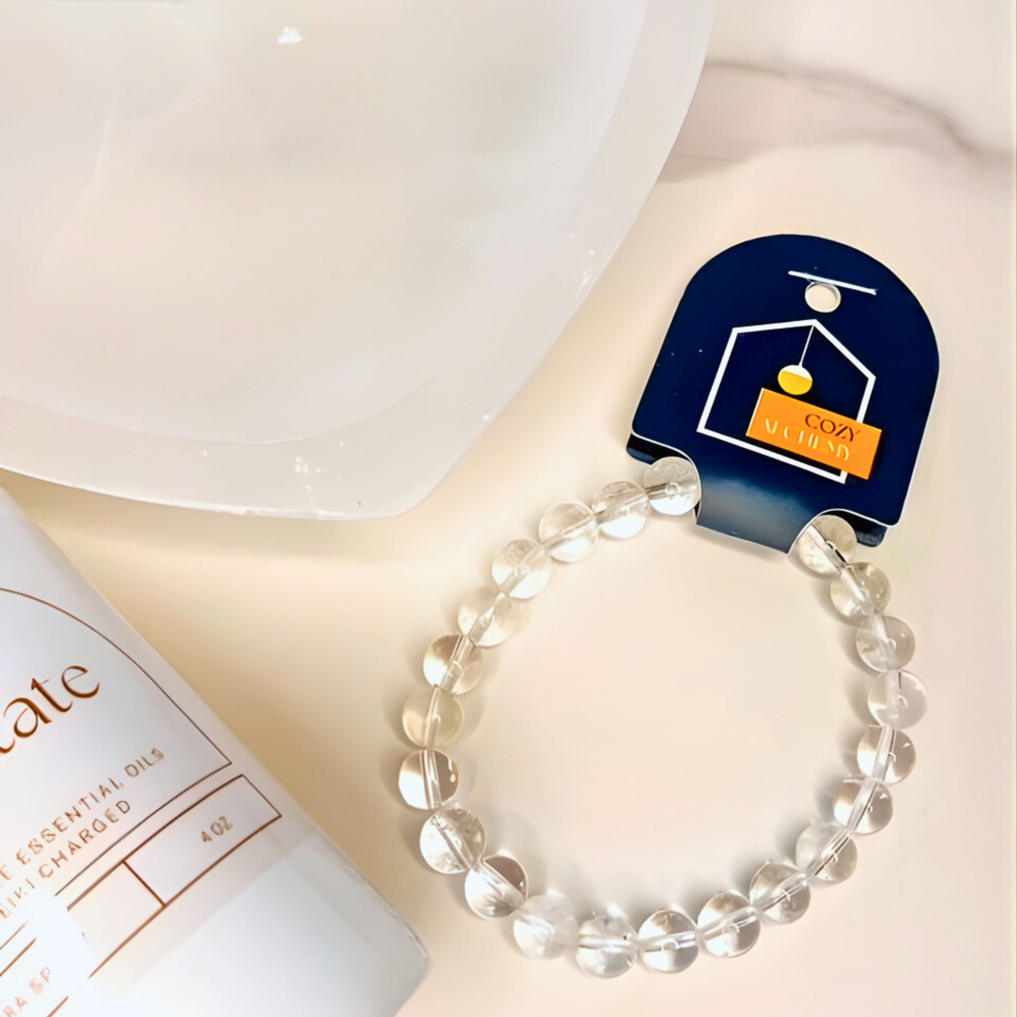 Clear beaded bracelet on a white surface with a Cozy & Cozy product packaging in the background.