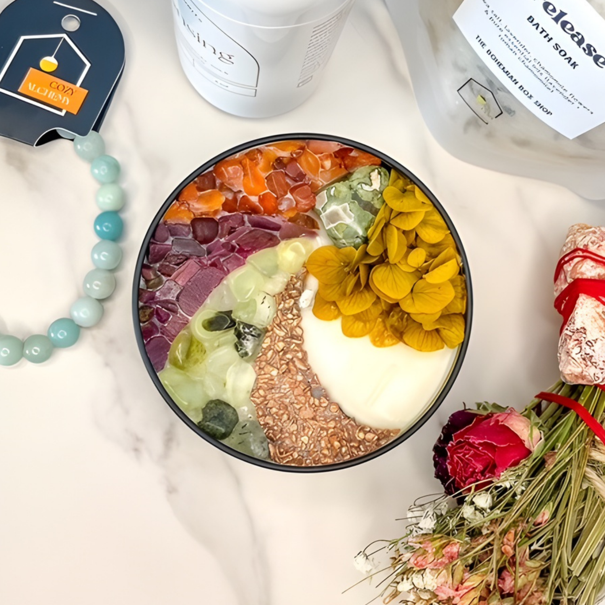 Colorful bath bomb in a black bowl with flowers and bath products on a marble surface