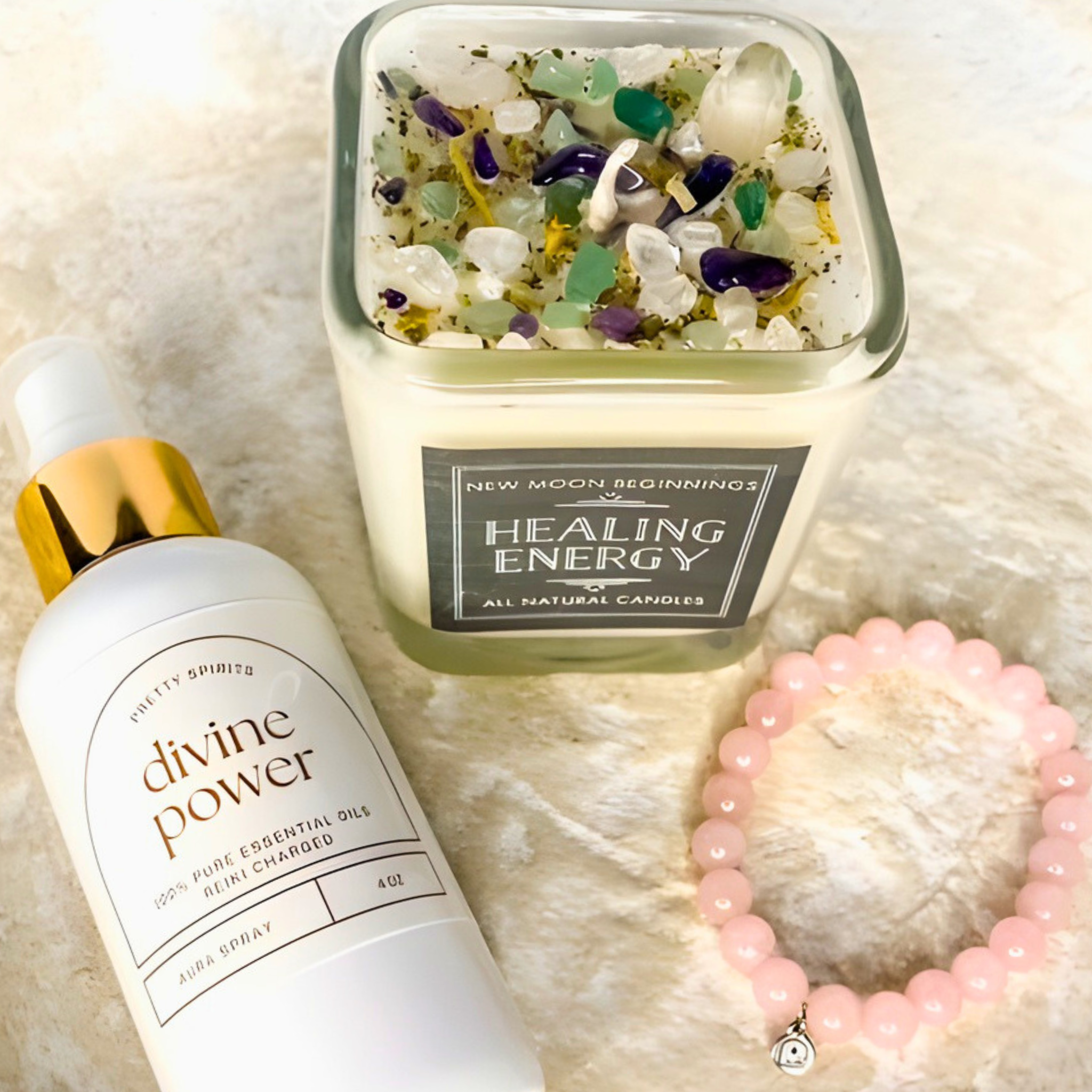 Candle labeled 'Healing Energy' with a bottle labeled 'divine power' and a pink beaded bracelet on a textured surface.