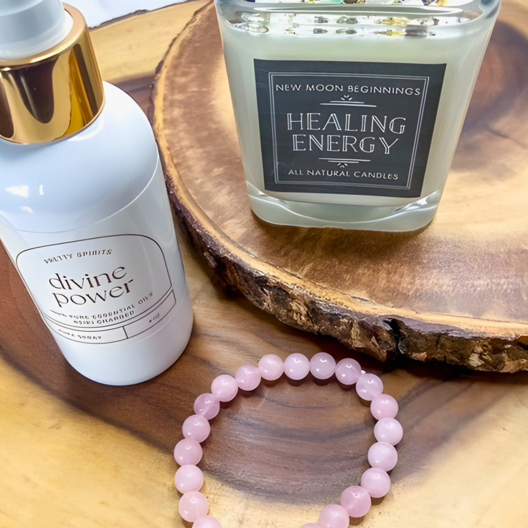 Bottle labeled 'divine power', candle labeled 'Healing Energy', and pink beaded bracelet on a wooden surface
