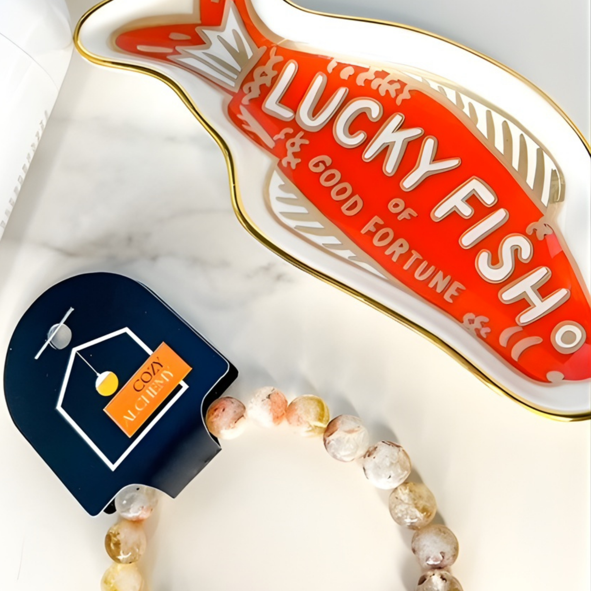 Decorative item with 'Lucky Fish' tag and a bracelet on a marble surface