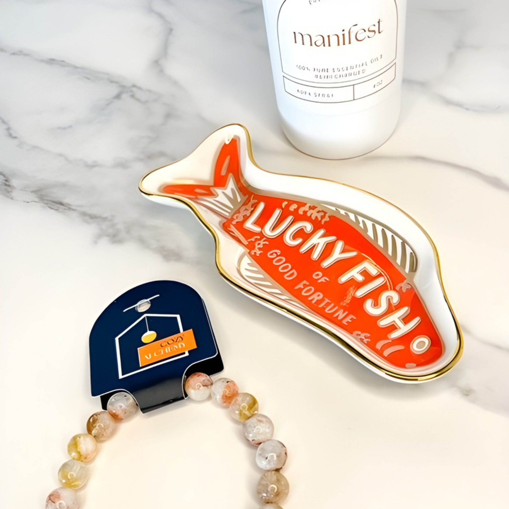 Lucky Fish charm on a marble surface with a bottle labeled 'manifest'.