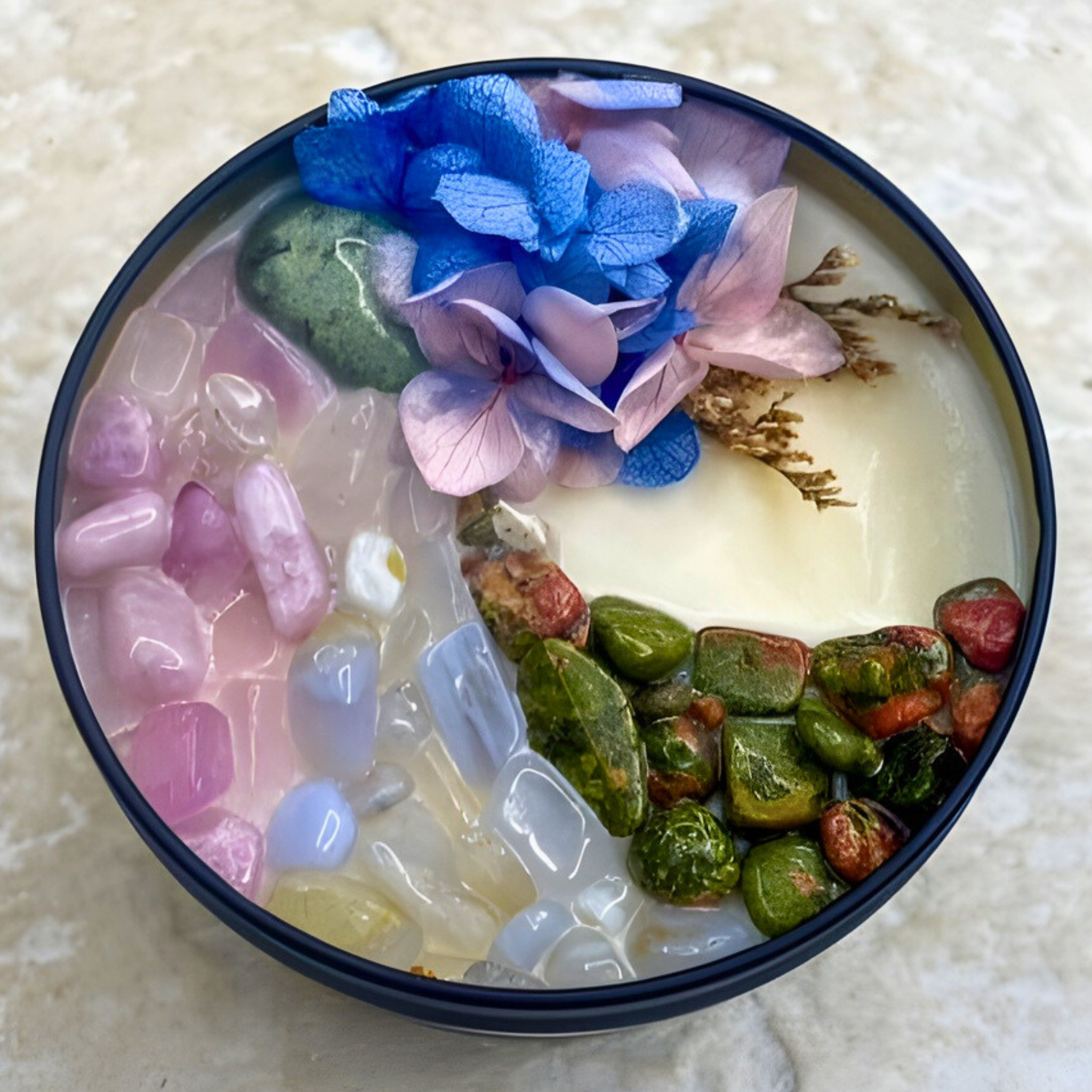 Decorative bowl with colorful stones and flowers on a textured surface