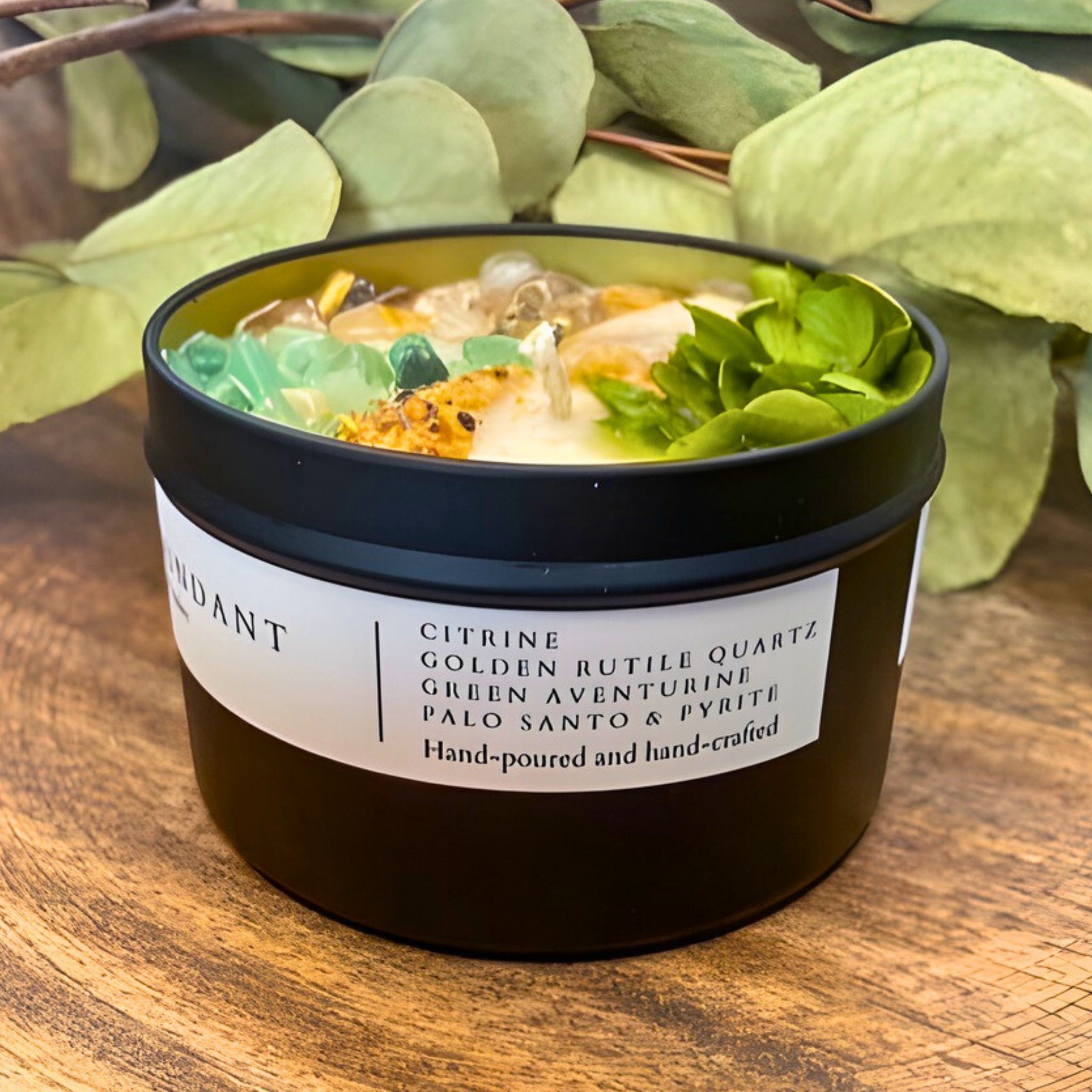 Black container with decorative stones and leaves on a wooden surface, featuring a label with text.