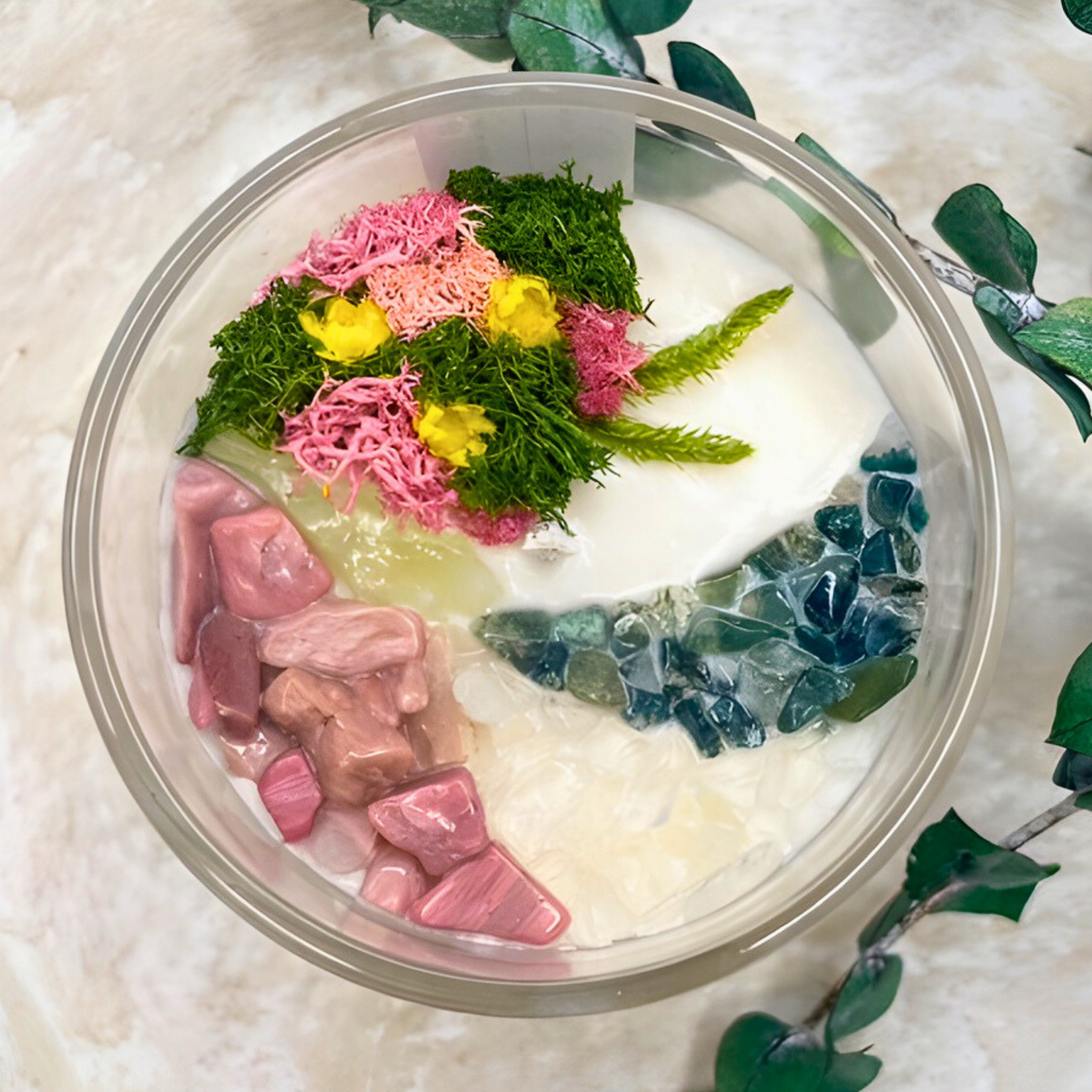 Decorative arrangement with pink and green elements in a clear container on a textured surface.