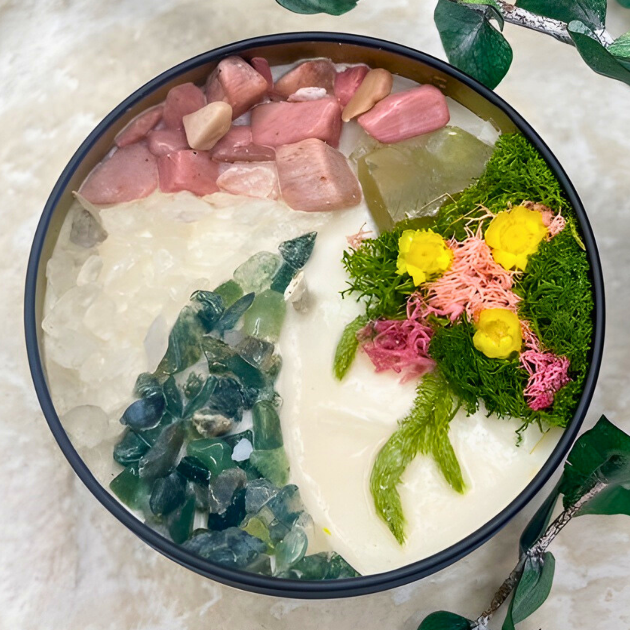 Decorative bowl with stones, flowers, and greenery on a textured surface