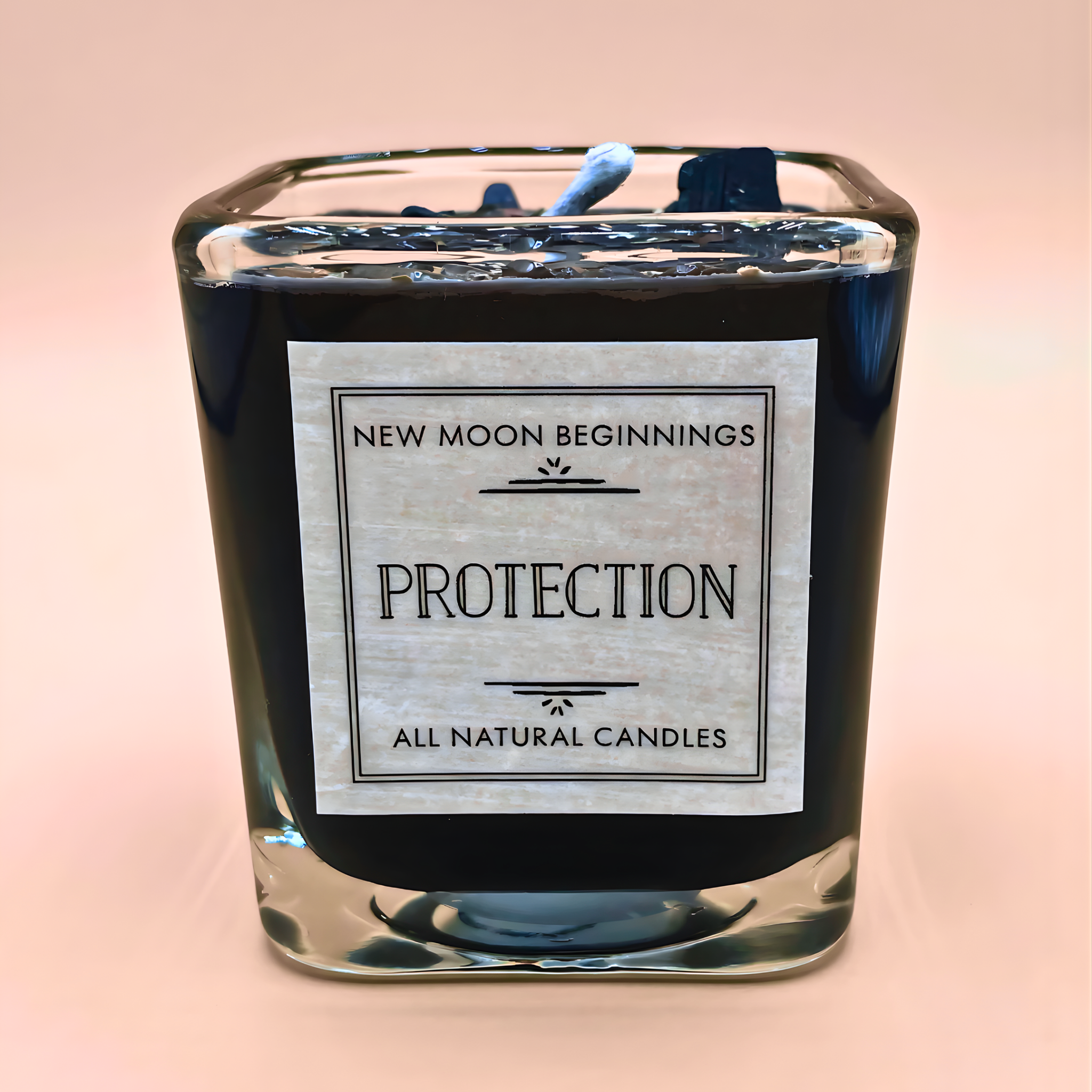 Candle with a label reading 'New Moon Beginnings Protection All Natural Candles' on a pink background
