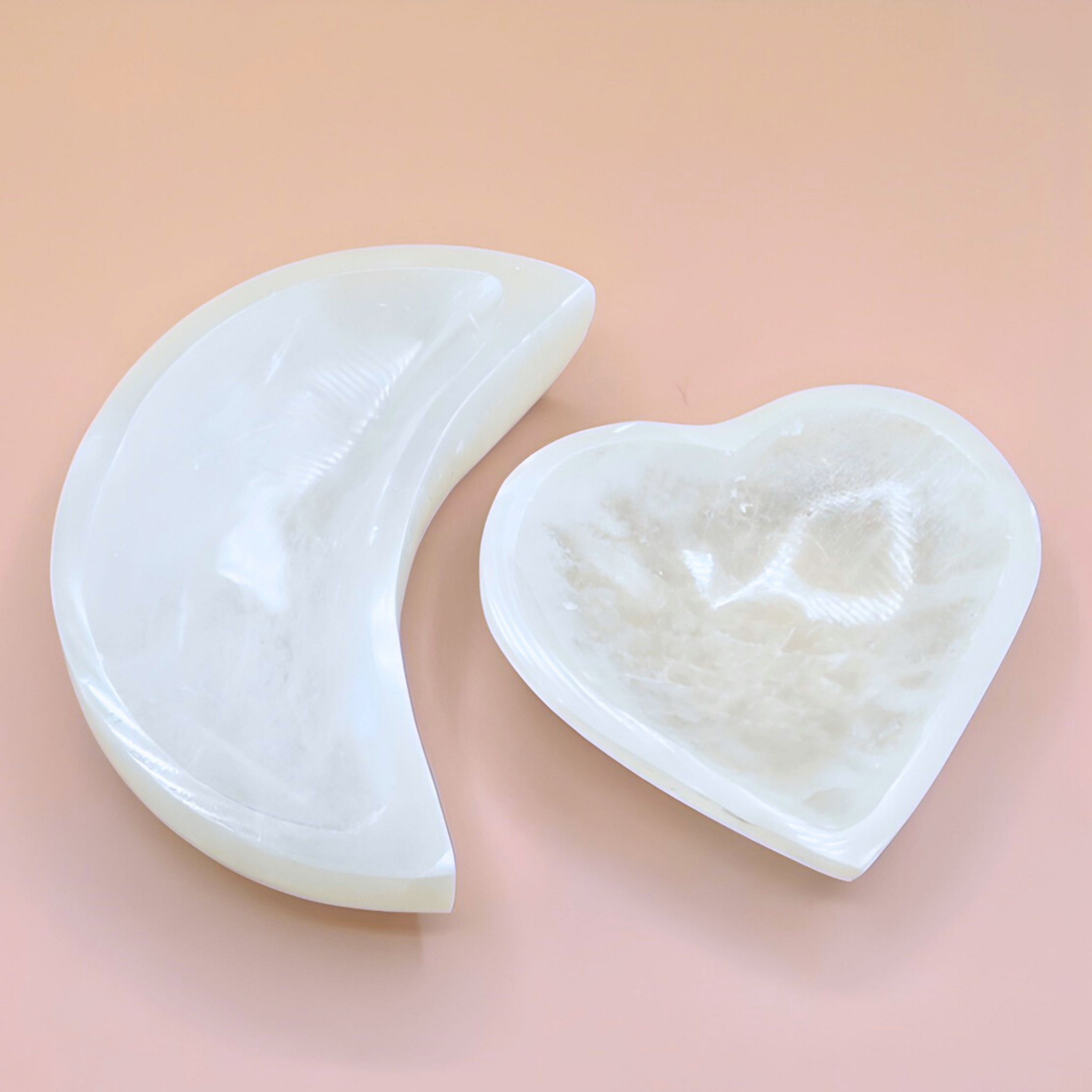 Two white jade heart-shaped tools on a light pink background