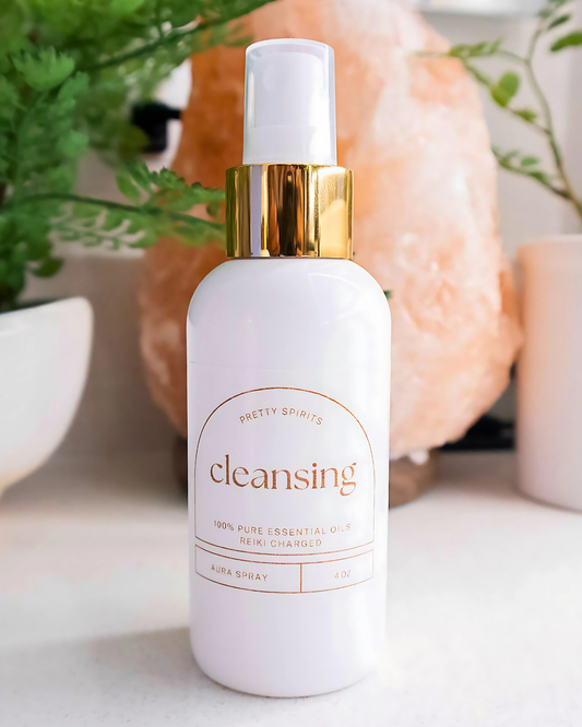 White cleansing spray bottle with gold cap on a white surface with plants in the background