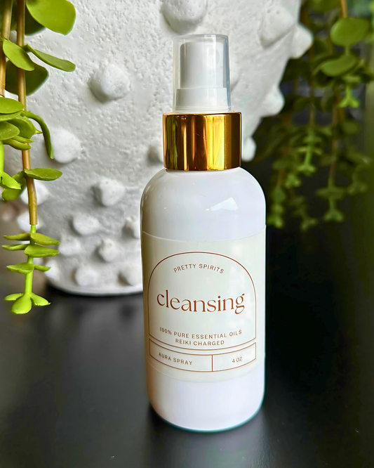White bottle with gold cap labeled 'cleansing' on a dark surface with greenery in the background