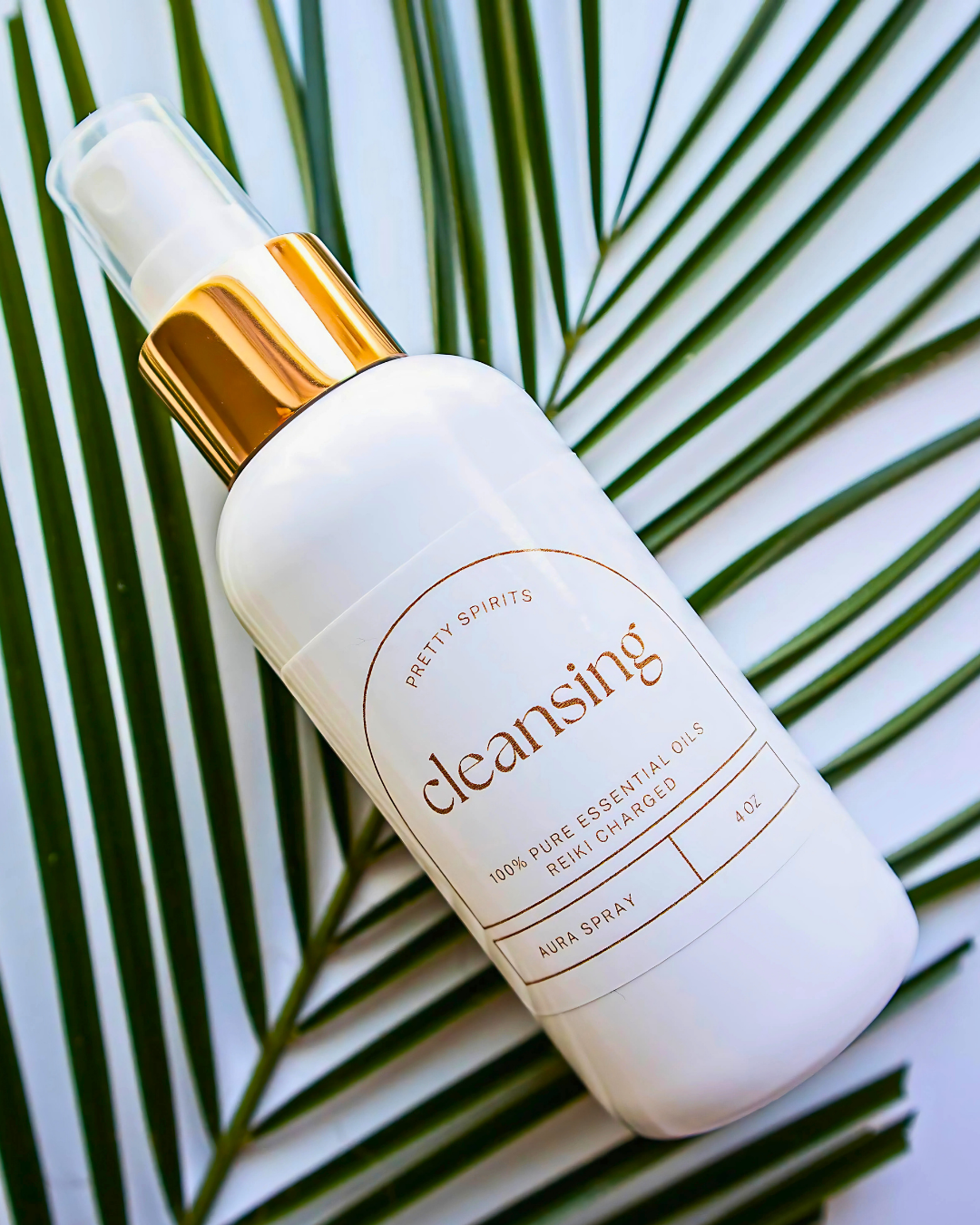 White bottle of 'Pretty Spirits' cleansing spray with gold cap on green leaf background