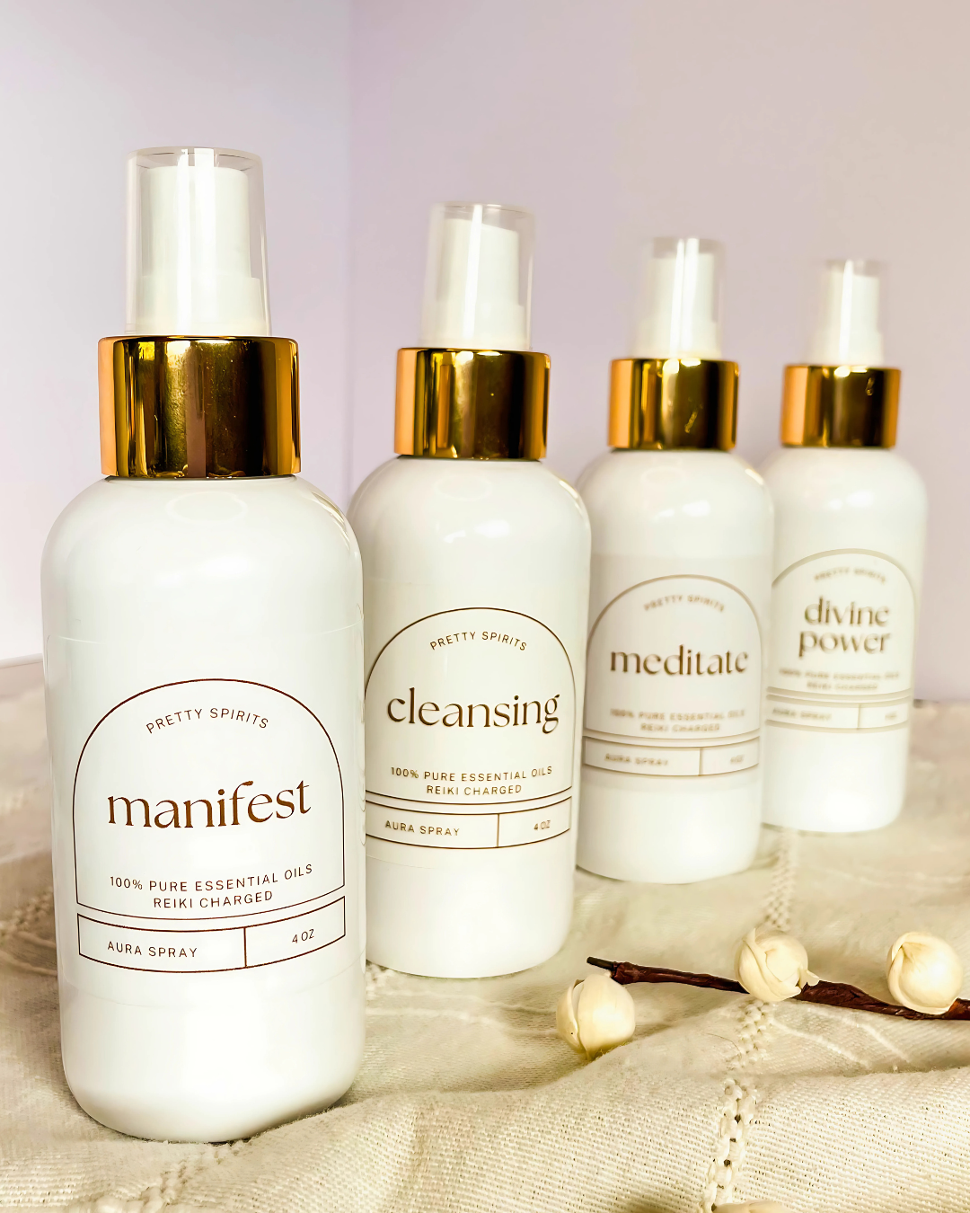 Four white essential oil bottles with gold caps on a soft fabric background