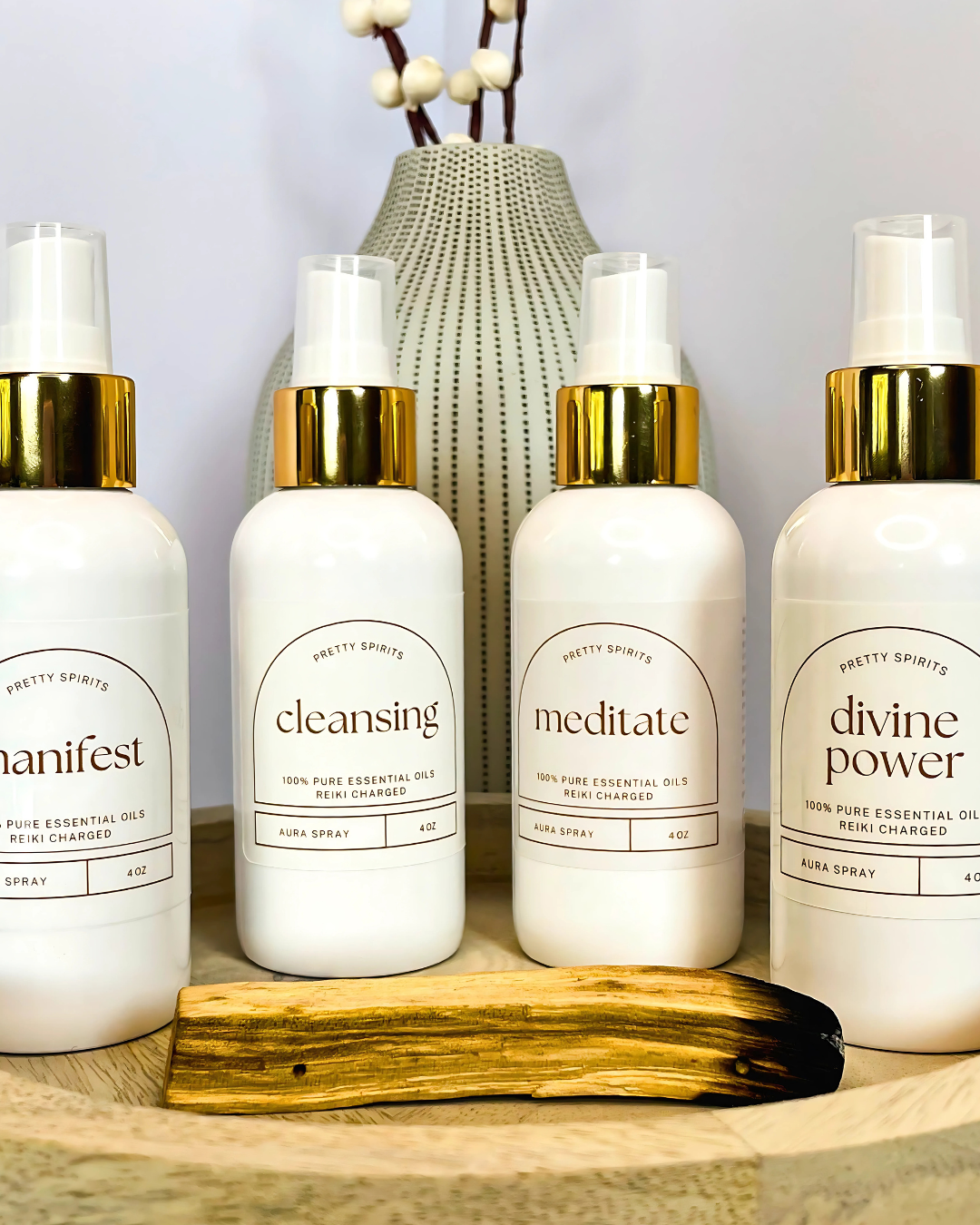 Four bottles of 'Pretty Spirits' essential oil sprays on a wooden surface with a vase in the background.