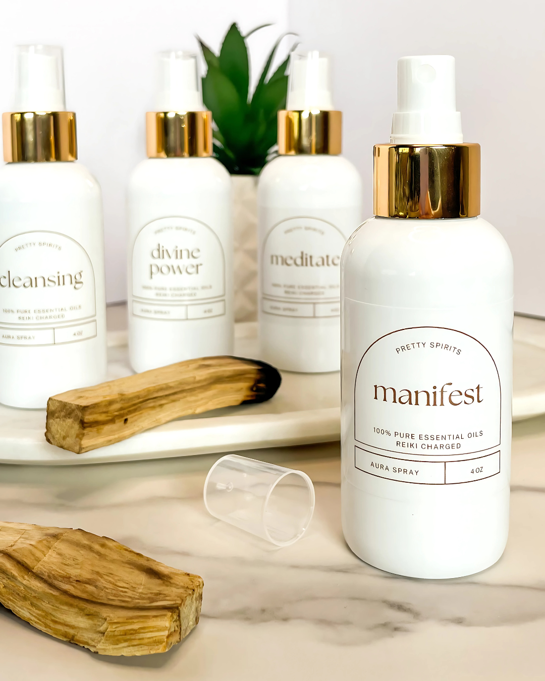 White essential oil bottles with gold caps on a marble surface, surrounded by wooden tools and greenery.